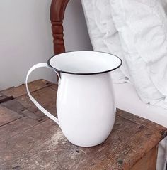 a white pitcher sitting on top of a wooden table next to a pillow and chair