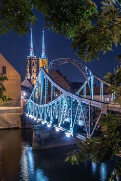 the bridge is lit up with blue lights on it's sides and there are buildings in the background