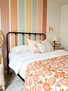 a bed with white sheets and pillows in a bedroom next to a colorful striped wall