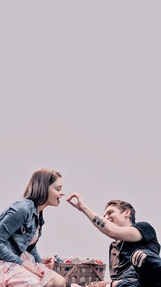 a man sitting on the ground next to a woman who is touching her nose with both hands