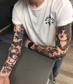 a man with tattoos on his arm sitting in front of a table and holding a laptop