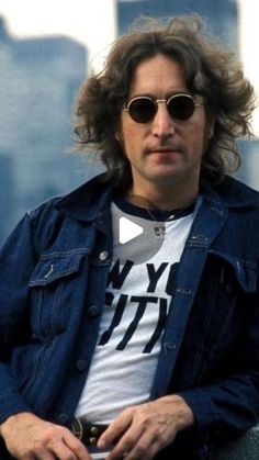 a man with long hair and sunglasses sitting on a bench in front of a cityscape