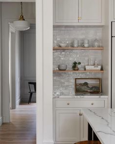 a kitchen with white cabinets and marble counter tops, along with an open shelf on the wall