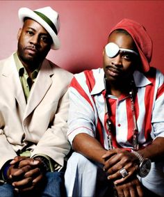 two men sitting next to each other in front of a red wall and wearing sunglasses