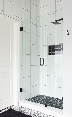 a bathroom with black and white tile on the floor, shower stall door and rug