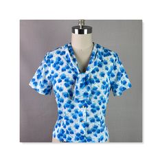 "Beautiful 50s blouse.  Fabric is a lightweight polyester dacron.  White background with little florals in two shades of blue. Low front neckline with attached tie.  Button front with short sleeves. Excellent condition with no issues. Label is Modes de Paris, Made in California. No size is indicated so please check the measurements carefully. *bust 36\" *waist 32\" *shoulders 15 1/2\" *length 20\" Alley Cats Vintage is a Member of the Vintage Fashion Guild." Blue Collar Top With Floral Print, Blue Floral Print Top With Collar, Fitted Floral Print Blouse With Tie Neck, Fitted Floral Print Top With Peter Pan Collar, Vintage Blue Short Sleeve Blouse, Blue Fitted Tie Neck Tops, Blue Fitted Tie Neck Blouse, Blue Fitted Blouse With Tie Neck, Retro Fitted Short Sleeve Blouse