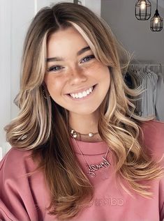 a woman with long blonde hair smiling at the camera and wearing a pink sweatshirt in front of a closet