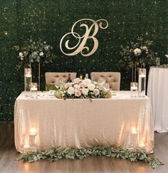 a table with candles and flowers on it in front of a wall covered in greenery