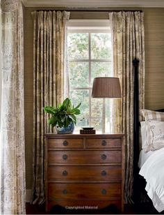 a bed sitting next to a wooden dresser in front of a window with drapes