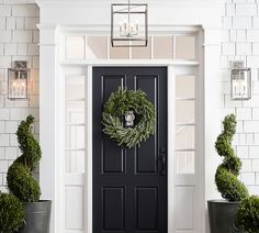 a black front door with a wreath and two potted plants on the side walk