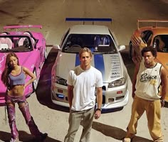 three men and two women standing in front of four different colored sports cars with the hood up