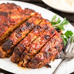 meatloaf with sauce and parsley on a white plate next to a fork