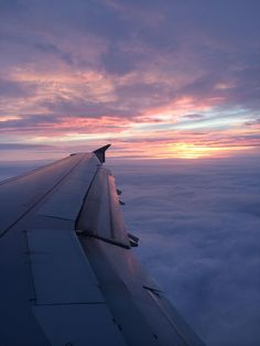 the wing of an airplane as it flies above the clouds at sunset or dawn in the sky