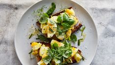 a white plate topped with toast covered in eggs and spinach on top of a table