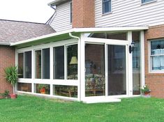 a large white sunroom sitting on top of a lush green field next to a house