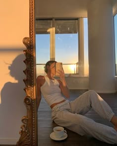 a woman sitting on the floor taking a selfie in front of a large mirror