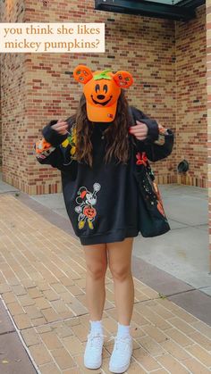 a woman wearing an orange pumpkin hat and black sweatshirt with mickey mouse ears on her head