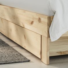 a wooden bed frame with white sheets and pillows on it's headboard, next to a rug