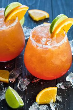 two orange margaritas with lime wedges on the rim and ice cubes around them