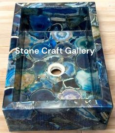 a blue glass sink sitting on top of a wooden table with the words stone craft gallery above it