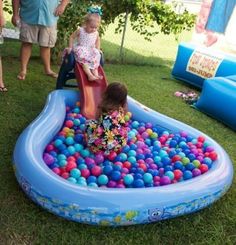 two children playing in an inflatable pool with balls on the ground and people standing around