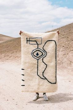 a person standing in the desert holding up a towel with an eye drawn on it