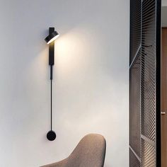 a modern wall light mounted on the side of a white wall next to a chair