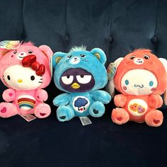 three hello kitty stuffed animals sitting next to each other on a blue couch with black velvet upholster