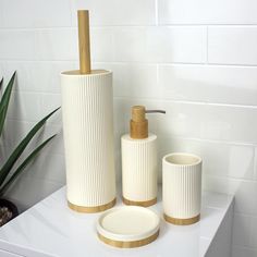 three white and gold bathroom accessories on top of a counter next to a potted plant