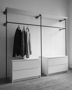 an open closet with clothes hanging on the rails and two white dressers next to it