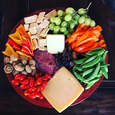 a red plate topped with lots of different types of cheeses and veggies