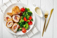 a white plate topped with meat and veggies next to a knife and fork