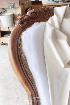 the back of a bed with white sheets on it and a wooden headboard that has an ornate carved frame