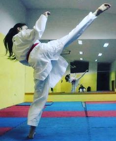 a woman is doing karate in a room with blue and red mats on the floor