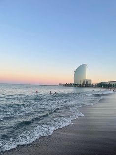 people are swimming in the ocean at sunset or sunrise on an empty beach with buildings in the background