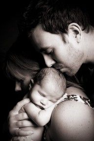 a black and white photo of a man kissing a woman's face while holding a baby