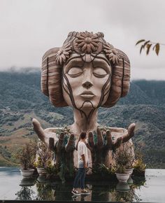 a man standing in front of a large statue with his hands on the water's surface