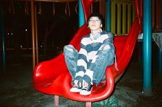 a young man sitting on top of a red slide in a playground at night time