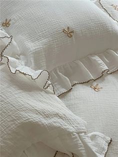 white bedding with gold embroidered details and ruffles on the bottom, along with two pillows