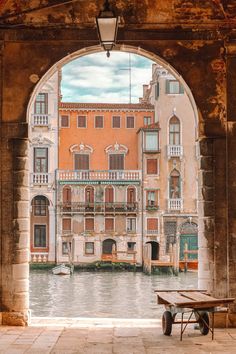 an archway leading to a building with boats in the water and a bench under it