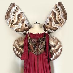 a dress made out of fabric with wings on the shoulders and chest, sitting on a mannequin's head