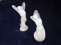 two white glass figurines sitting on top of a blue velvet covered tablecloth