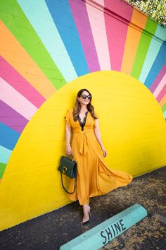 a woman in an orange dress leaning against a wall with the word shine painted on it