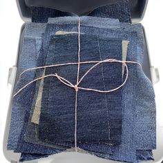 the inside of an open suitcase with some blue jeans in it and pink thread on top