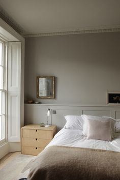 a bed with white sheets and pillows in a bedroom next to two large windows on the wall