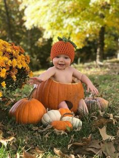 a baby in a pumpkin costume sitting on the ground with fall leaves and flowers around him