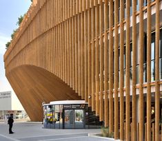 a bus parked in front of a building with wooden slats on the side and people standing outside