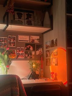 a desk with flowers and pictures on the wall above it, in a dimly lit room