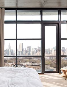 a bedroom with a bed, chair and large window looking out on the cityscape