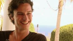 a young man smiling and wearing a necklace with flowers on it's neck, in front of a palm tree